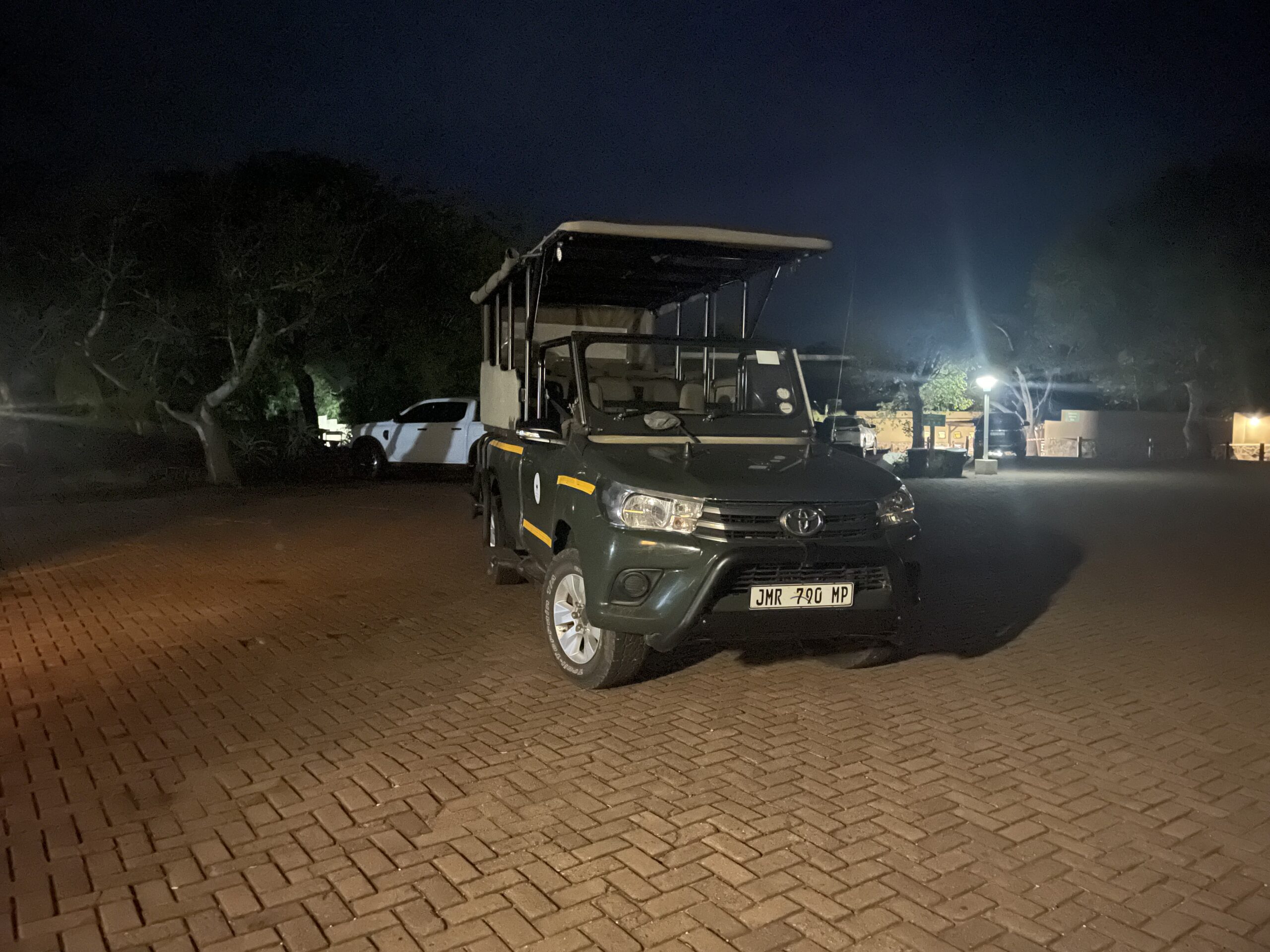 Ein Jeep mit Sitzen auf der Ladefäche und Überdachung, der im Dunkeln geparkt auf einem Parkplatz steht.